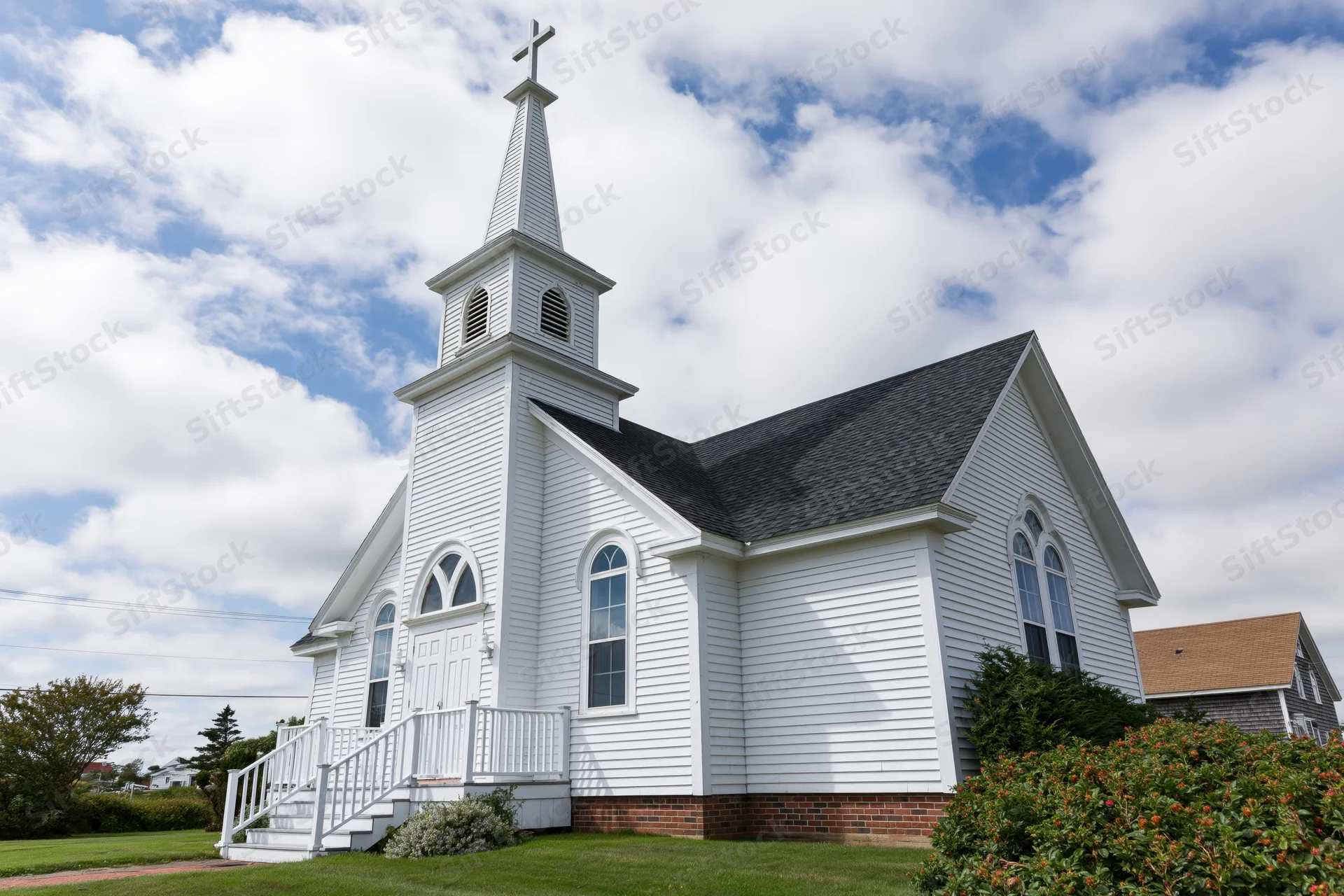 Small white clapboard church with tall steeple and cross under blue sky with clouds