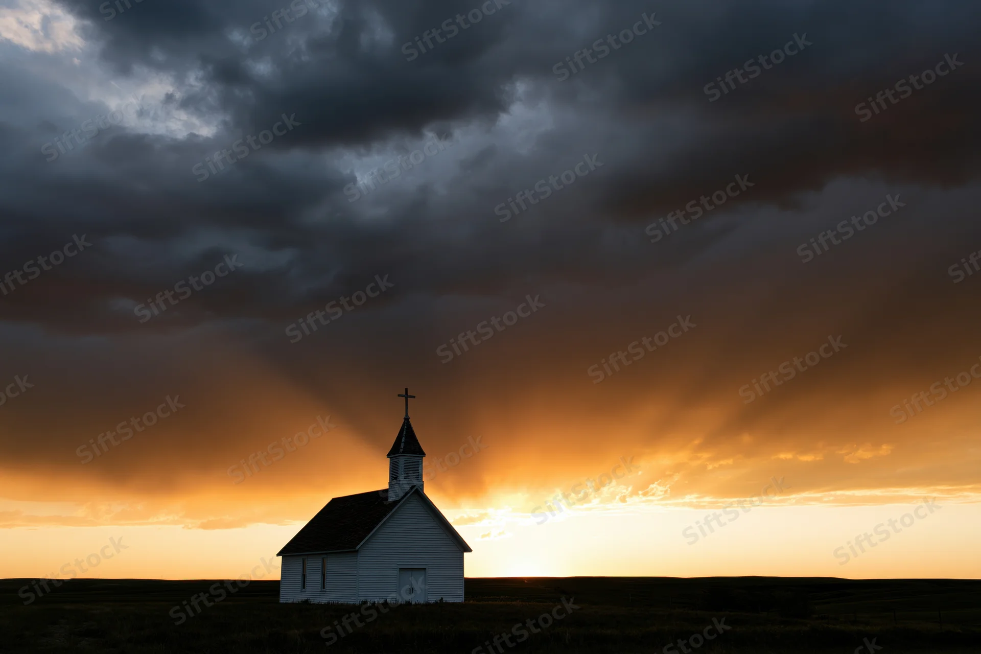 Small white country church silhouetted against dramatic sunset sky with sunbeams over open field