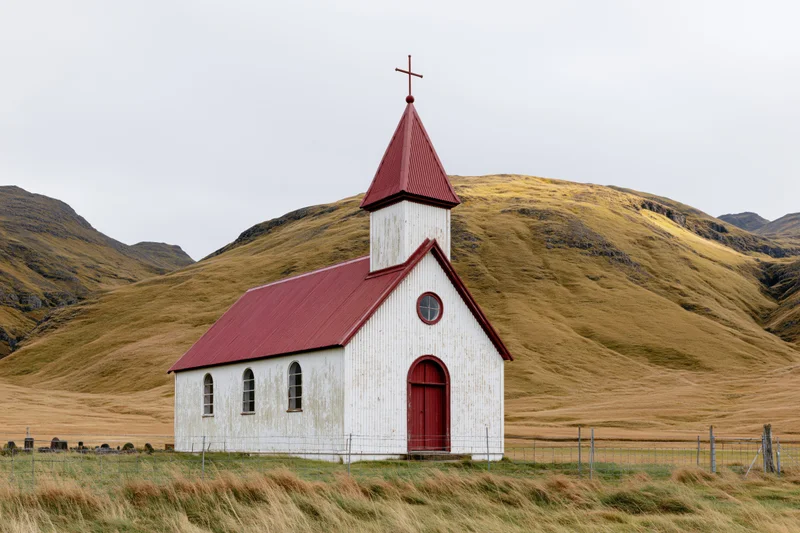 Small white rural church with red corrugated metal roof and steeple in a grassy field surrounded by rolling hills