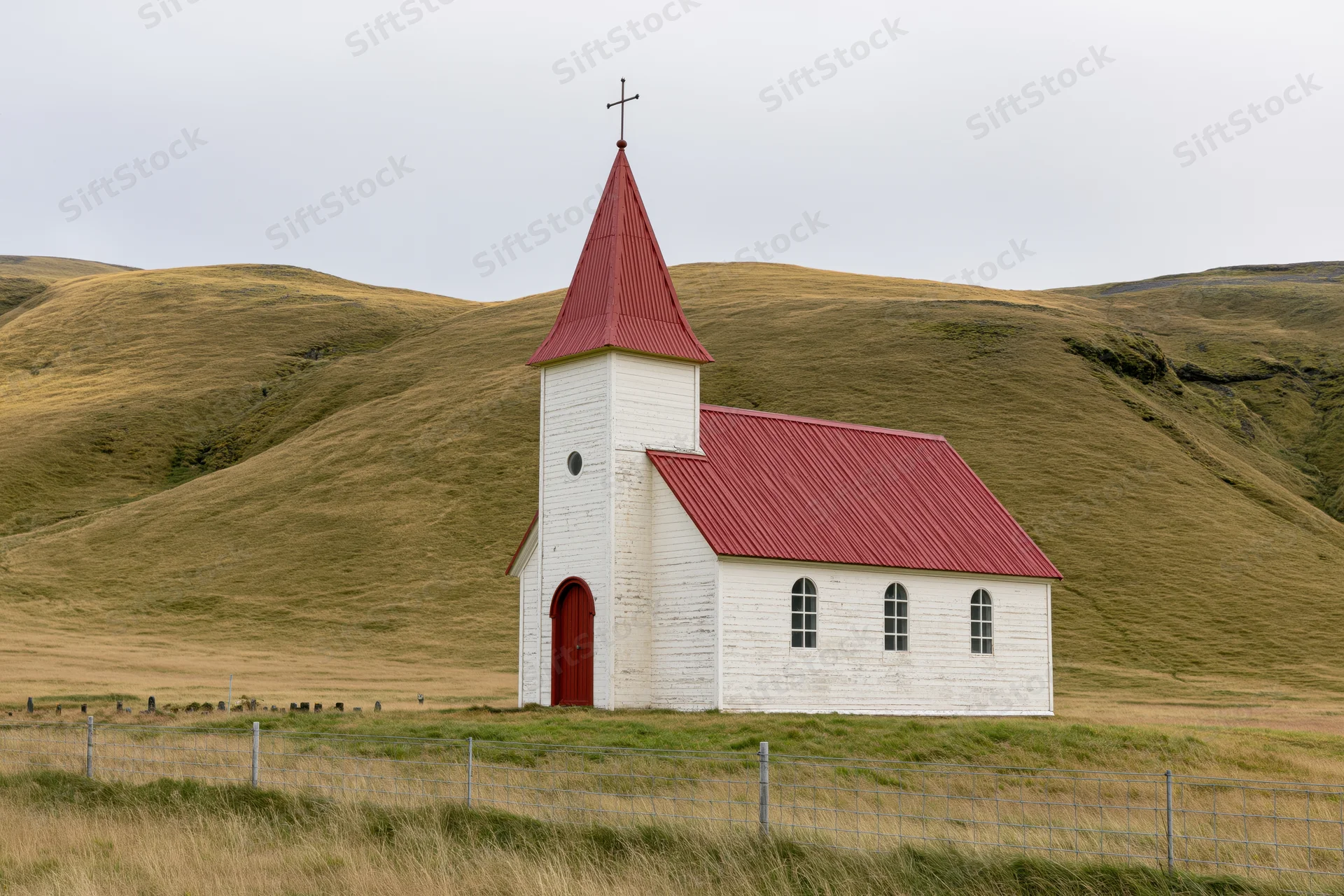 Small white rural church with red corrugated metal roof and steeple in a grassy hilly landscape