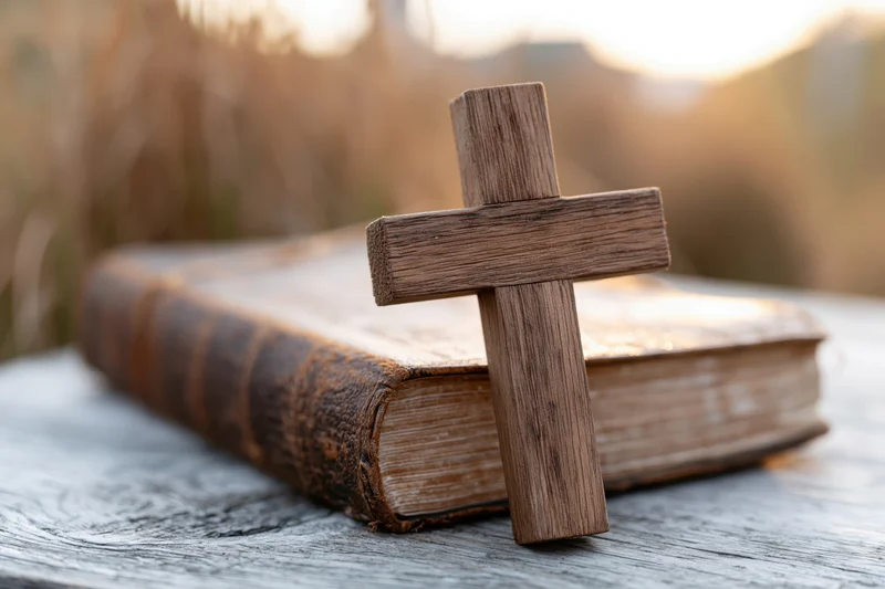 Wooden cross resting on an aged leather-bound bible outdoors at sunset