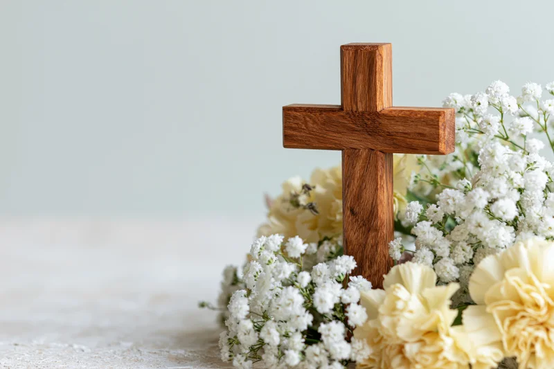 Wooden cross surrounded by white flowers and carnations on a light surface