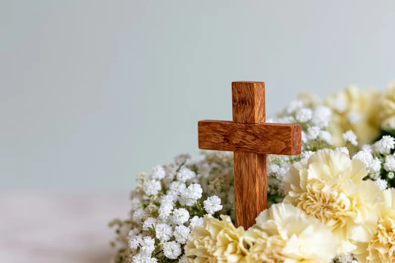 Wooden cross standing in a bouquet of white and cream flowers against a light background