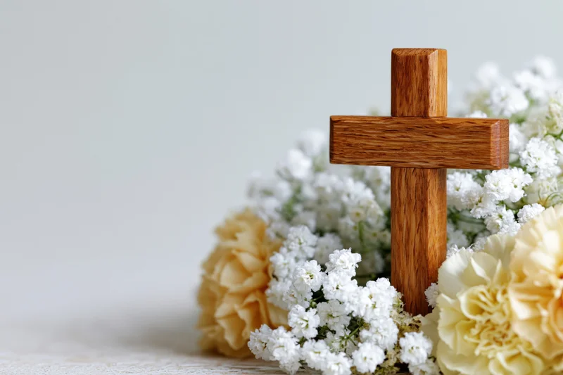 Wooden cross standing among white and cream flowers on a light surface