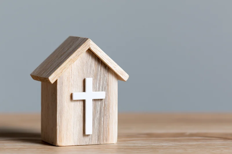 Wooden house-shaped block with white christian cross on wooden surface