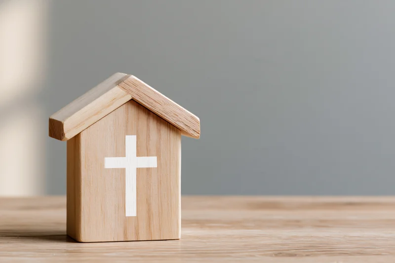 Wooden house-shaped block with white christian cross on tabletop