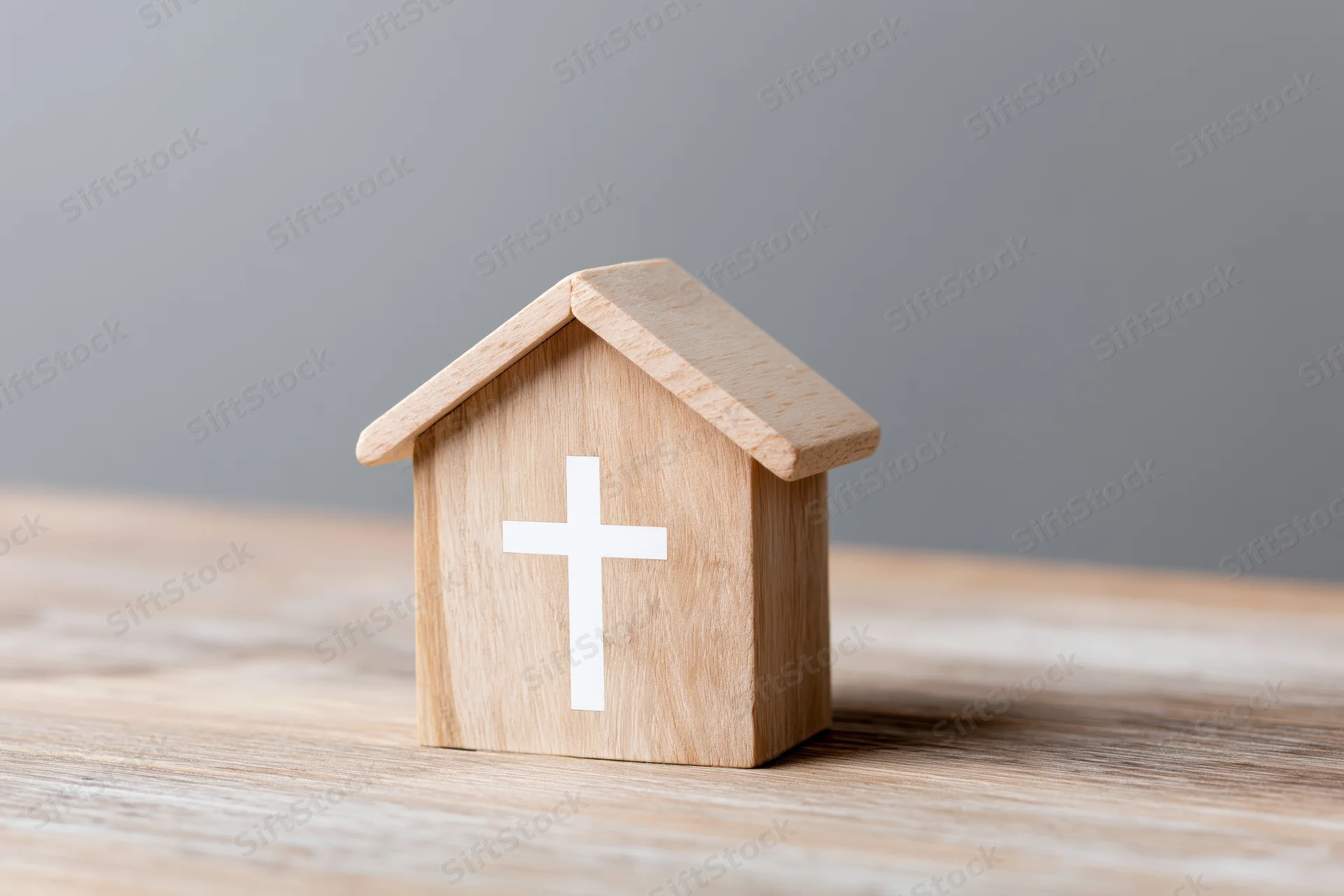 Wooden house block with white christian cross on wooden table