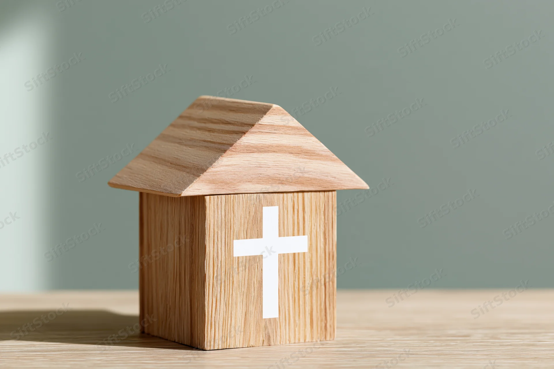 Wooden house-shaped block with white christian cross on a table