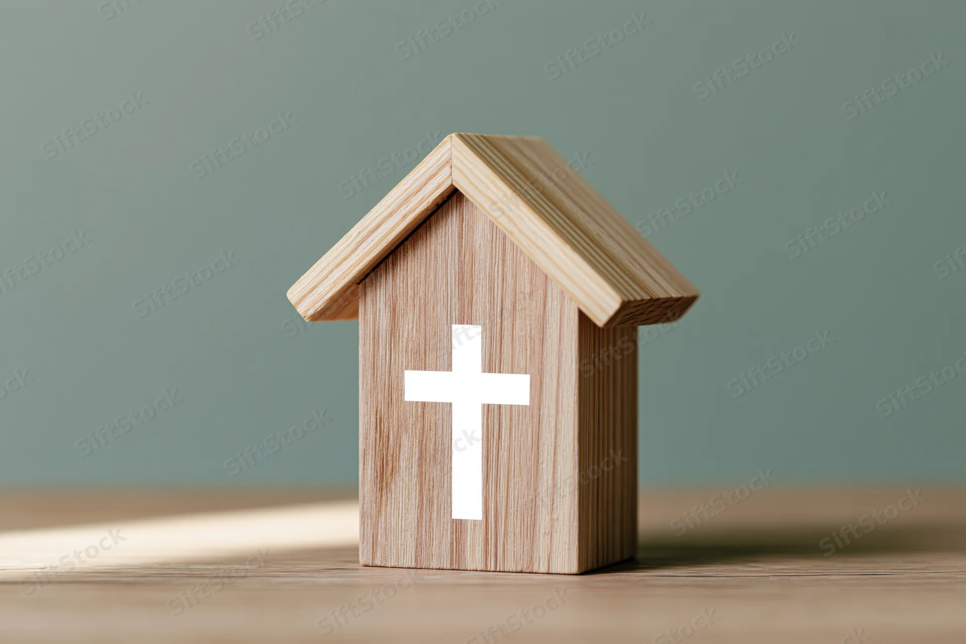Wooden house-shaped block with white christian cross on a table