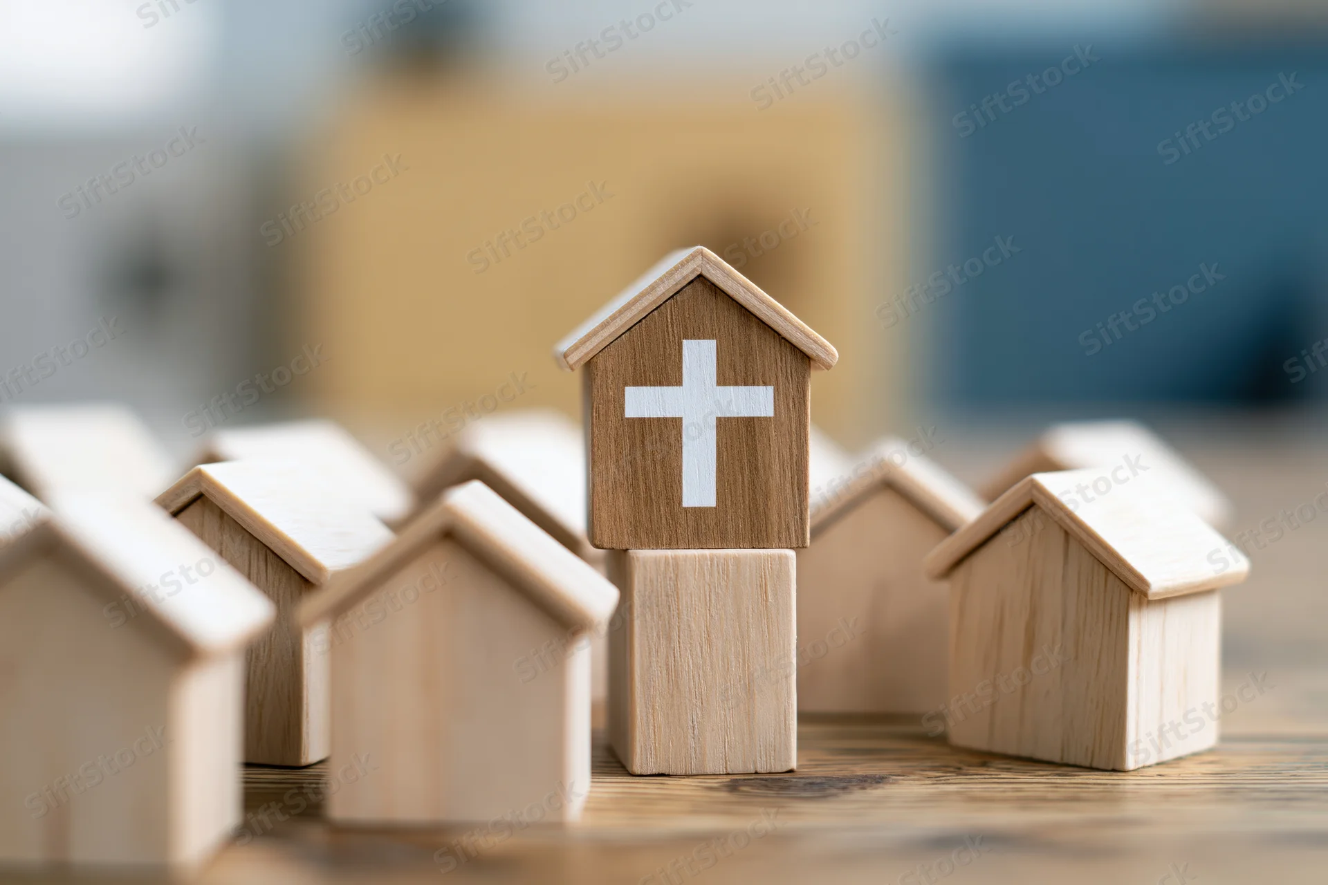 Wooden church model with white cross standing among other house blocks on a wooden surface