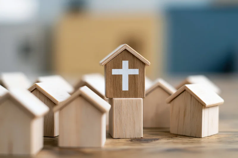 Wooden church model with white cross standing among other house blocks on a wooden surface