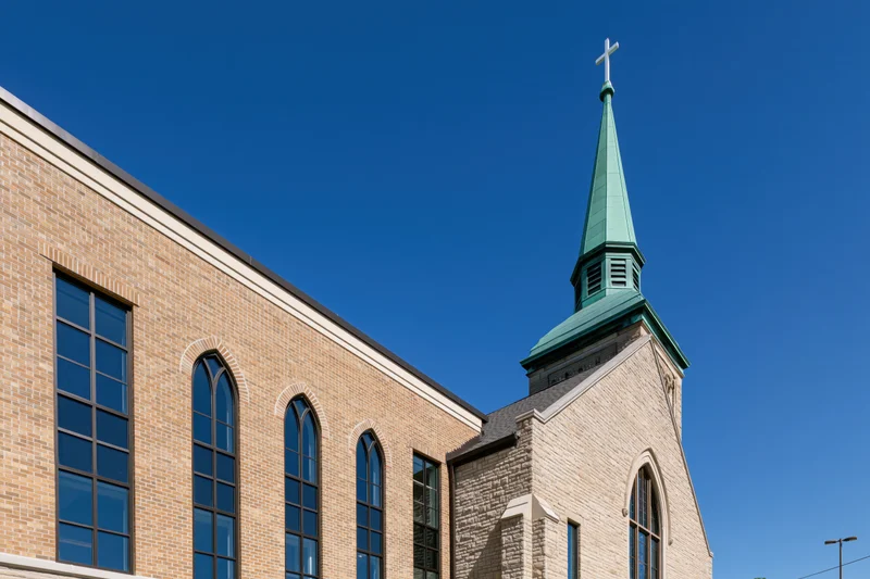 Suburban catholic church exterior with green copper steeple and arched windows under clear blue sky