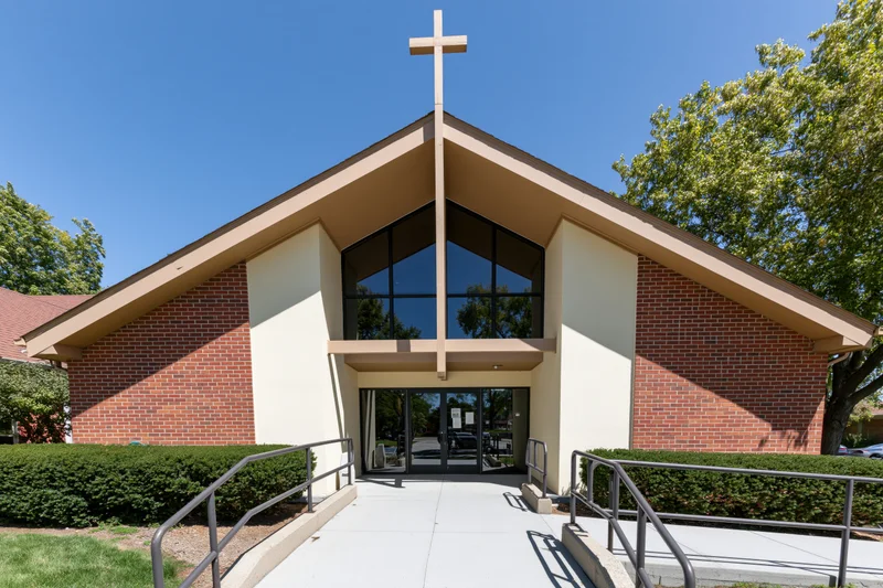 Suburban protestant church exterior with tall wooden cross above glass entrance and brick facade