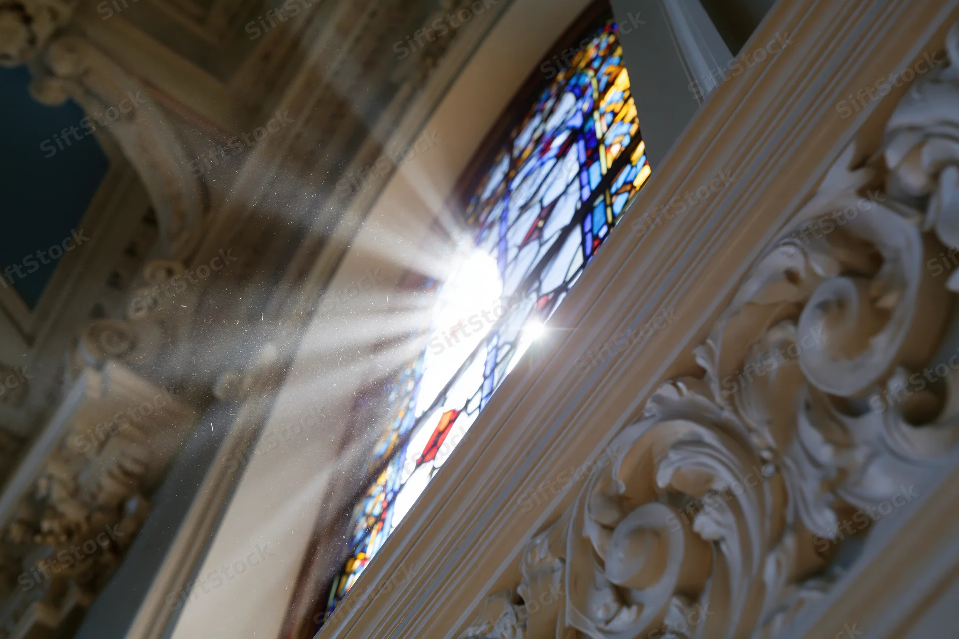 Sunlight bursting through a tall arched stained glass window in a church interior