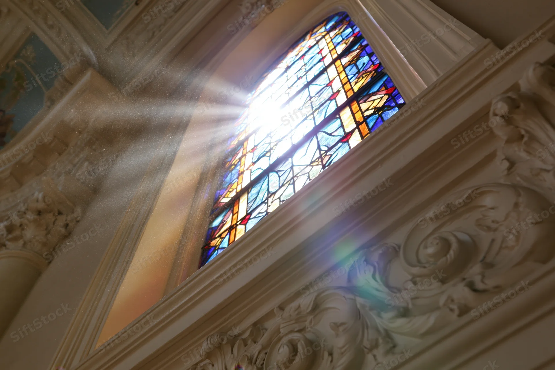 Sunlight bursting through a tall arched stained glass window in a church interior
