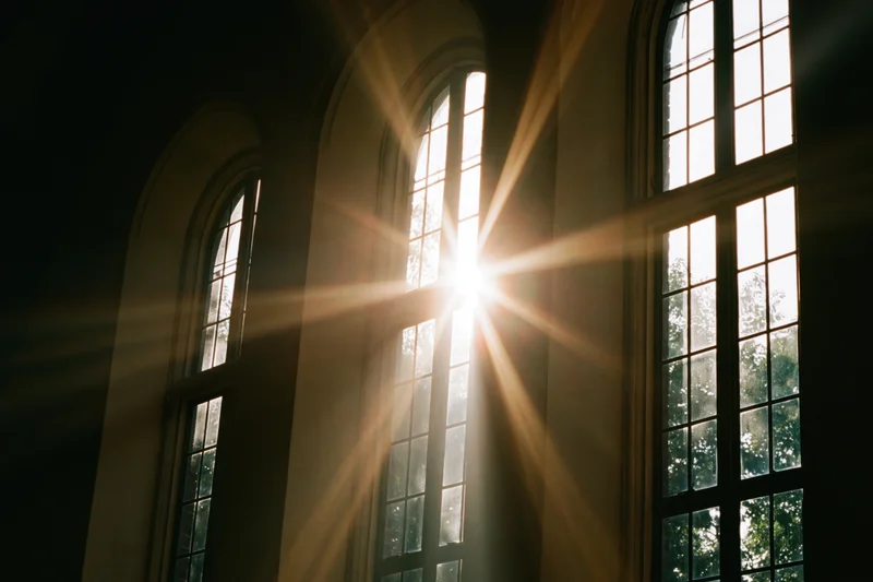 Sunlight bursting through tall arched church windows casting beams inside the interior