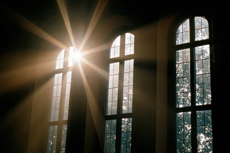 Sunlight bursting through tall arched church windows casting beams into the interior