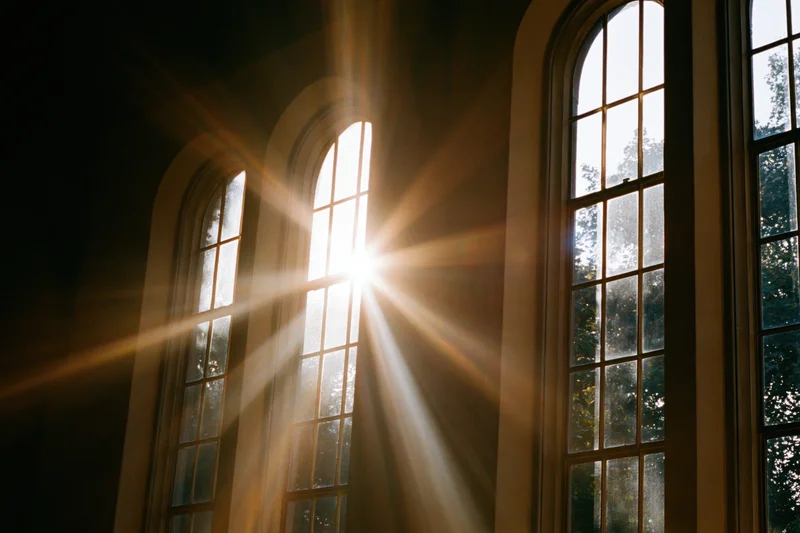 Sunlight bursting through tall arched church windows casting beams into the interior