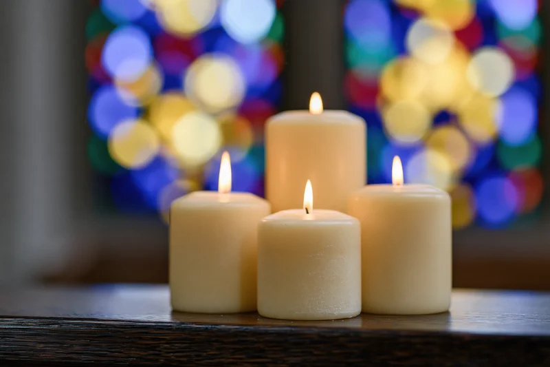 Four cream pillar candles burning on a wooden table with stained glass window bokeh in background