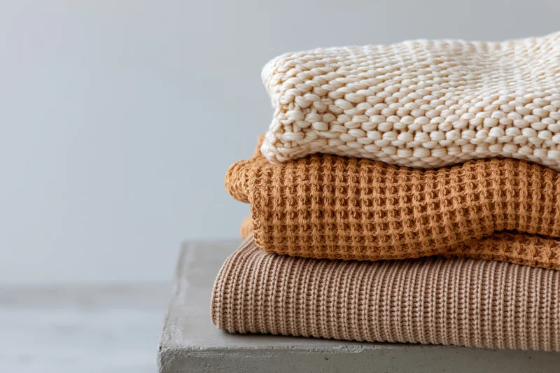 Three folded knit sweaters stacked on a concrete surface