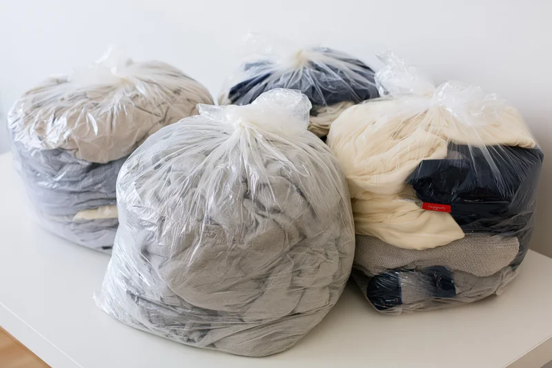 Several clear plastic bags filled with folded clothing arranged on a white table