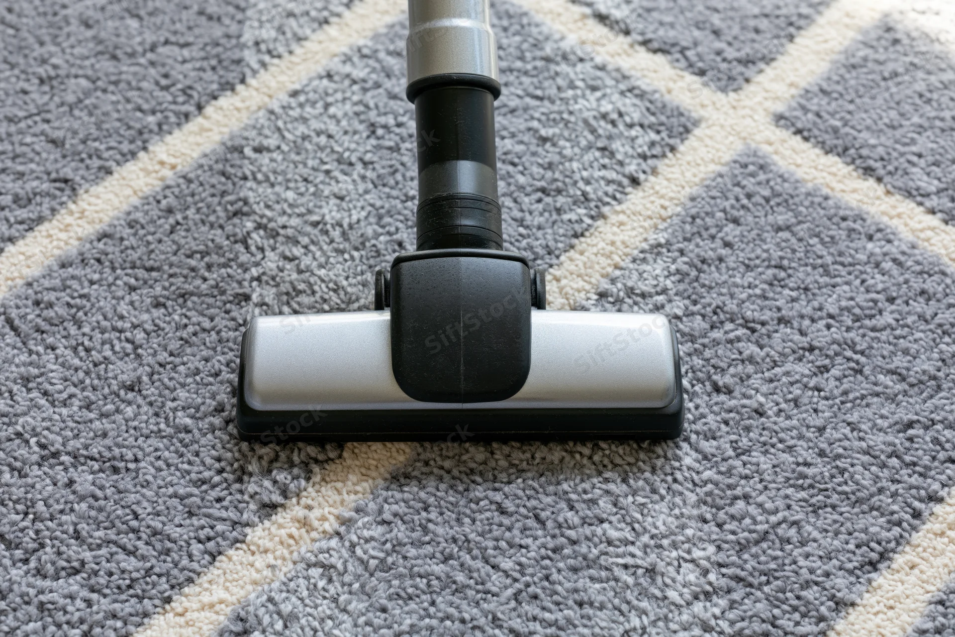 Vacuum cleaner head gliding across a gray geometric-patterned carpet in a home interior