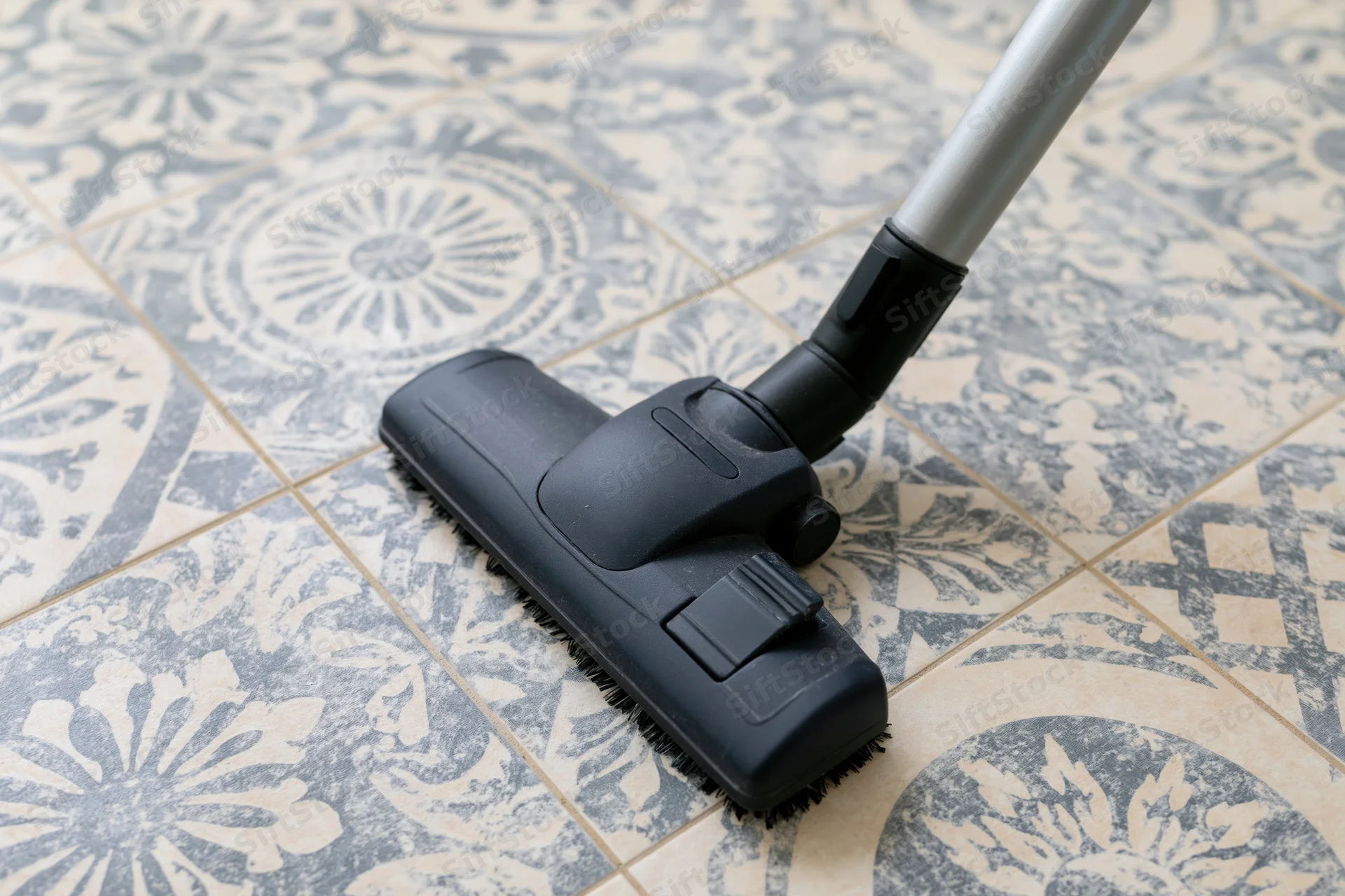 Vacuum cleaner head gliding across patterned ceramic floor tile