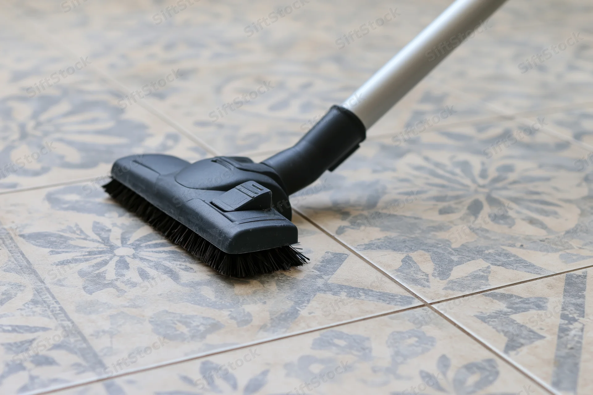Vacuum cleaner head gliding across patterned ceramic floor tiles