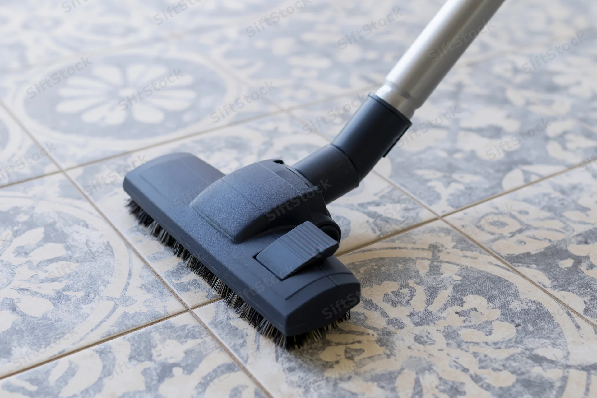 Vacuum cleaner head gliding across patterned ceramic floor tiles