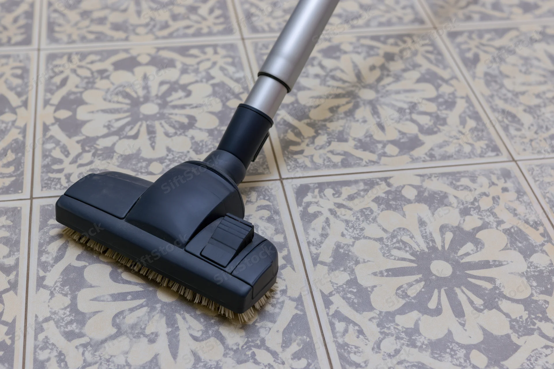 Vacuum cleaner head gliding across patterned ceramic floor tiles