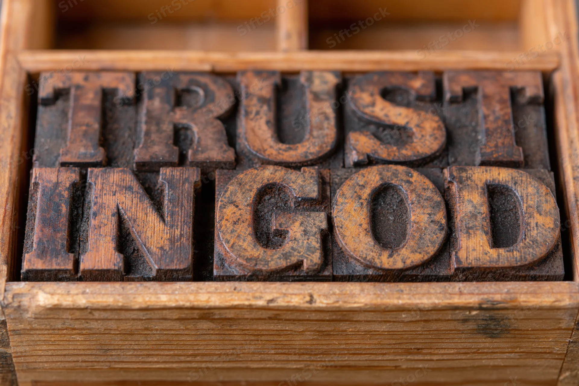 Vintage wooden letterpress blocks spelling trust in god arranged in a tray