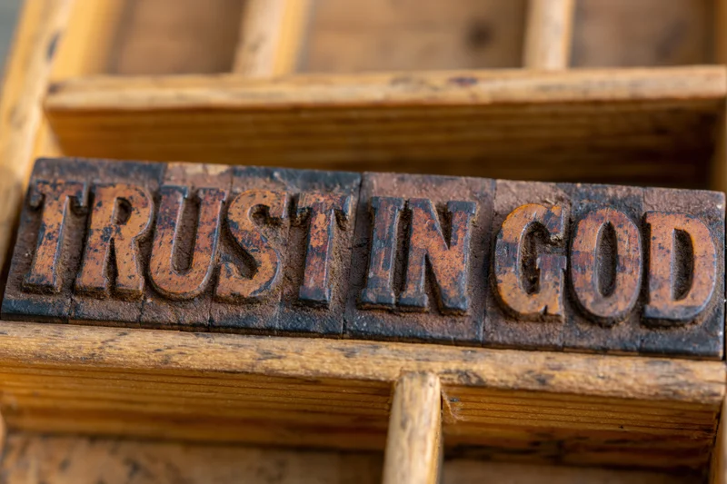 Vintage wooden letterpress blocks spelling trust in god arranged in a tray