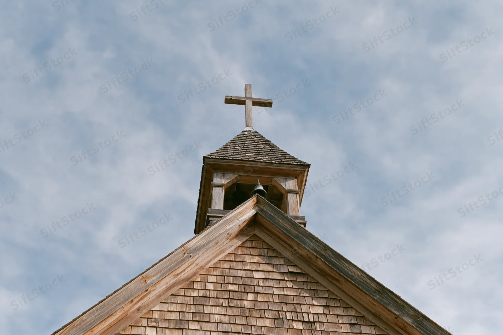 Wooden church steeple with cross against cloudy sky