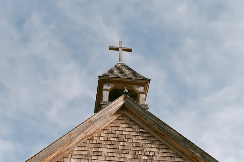 Wooden church steeple with cross against cloudy sky