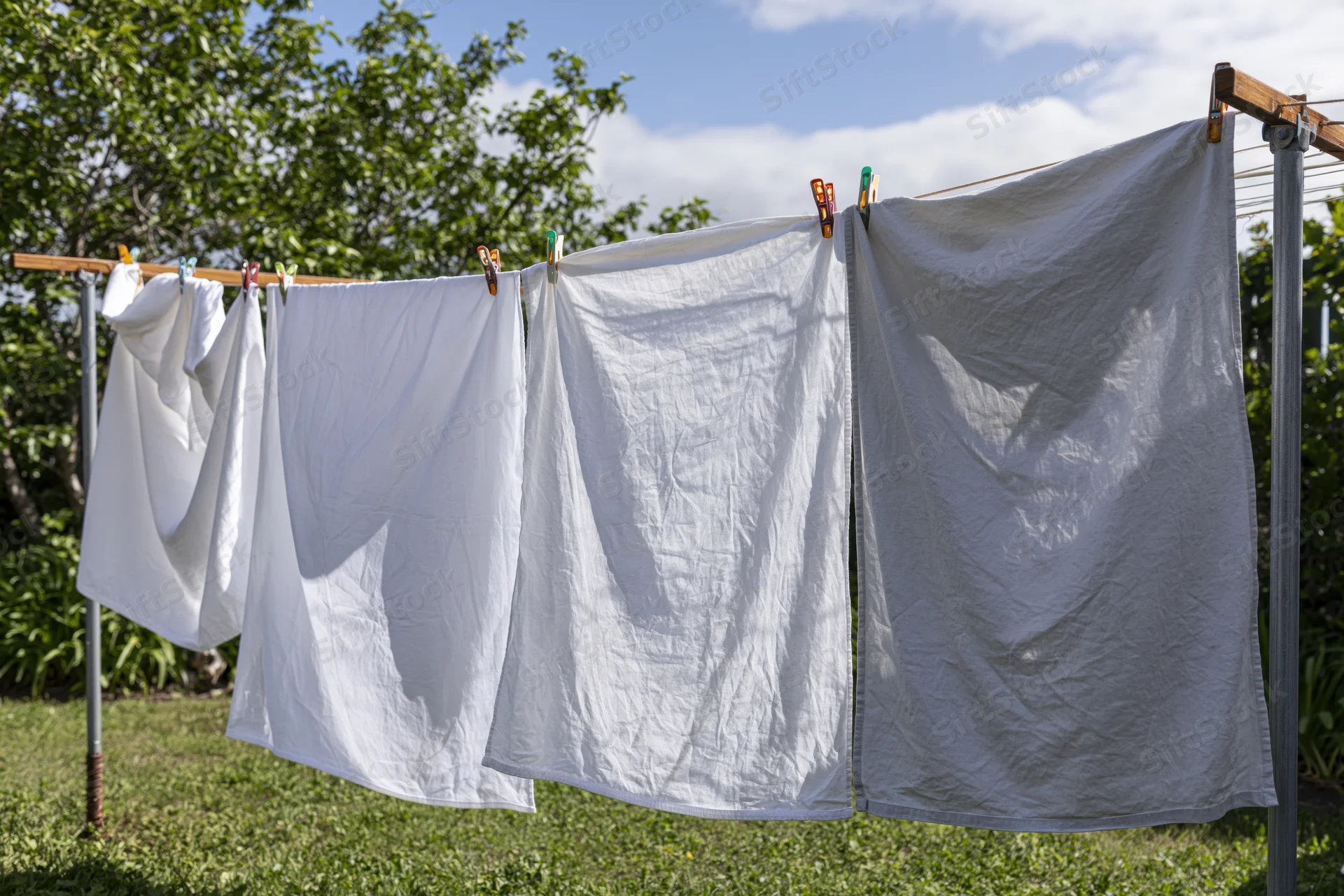 White and grey linens drying on a freestanding clothesline in a grassy garden under a partly cloudy sky