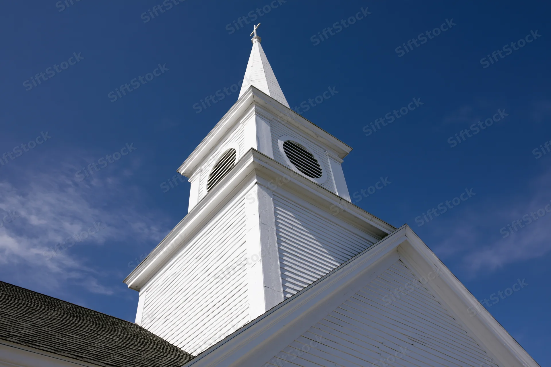 White church steeple with cross at peak against blue sky