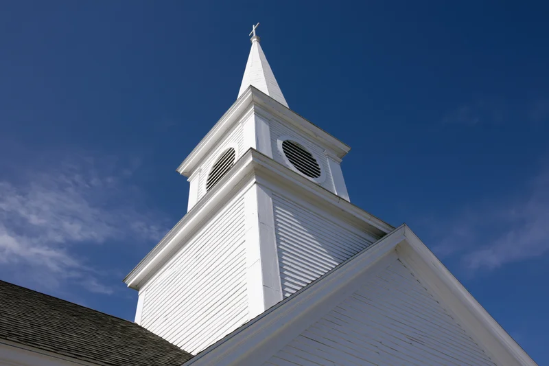 White church steeple with cross at peak against blue sky
