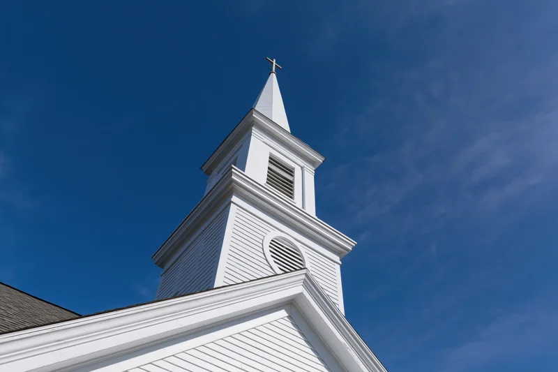 White church steeple with cross at peak against blue sky