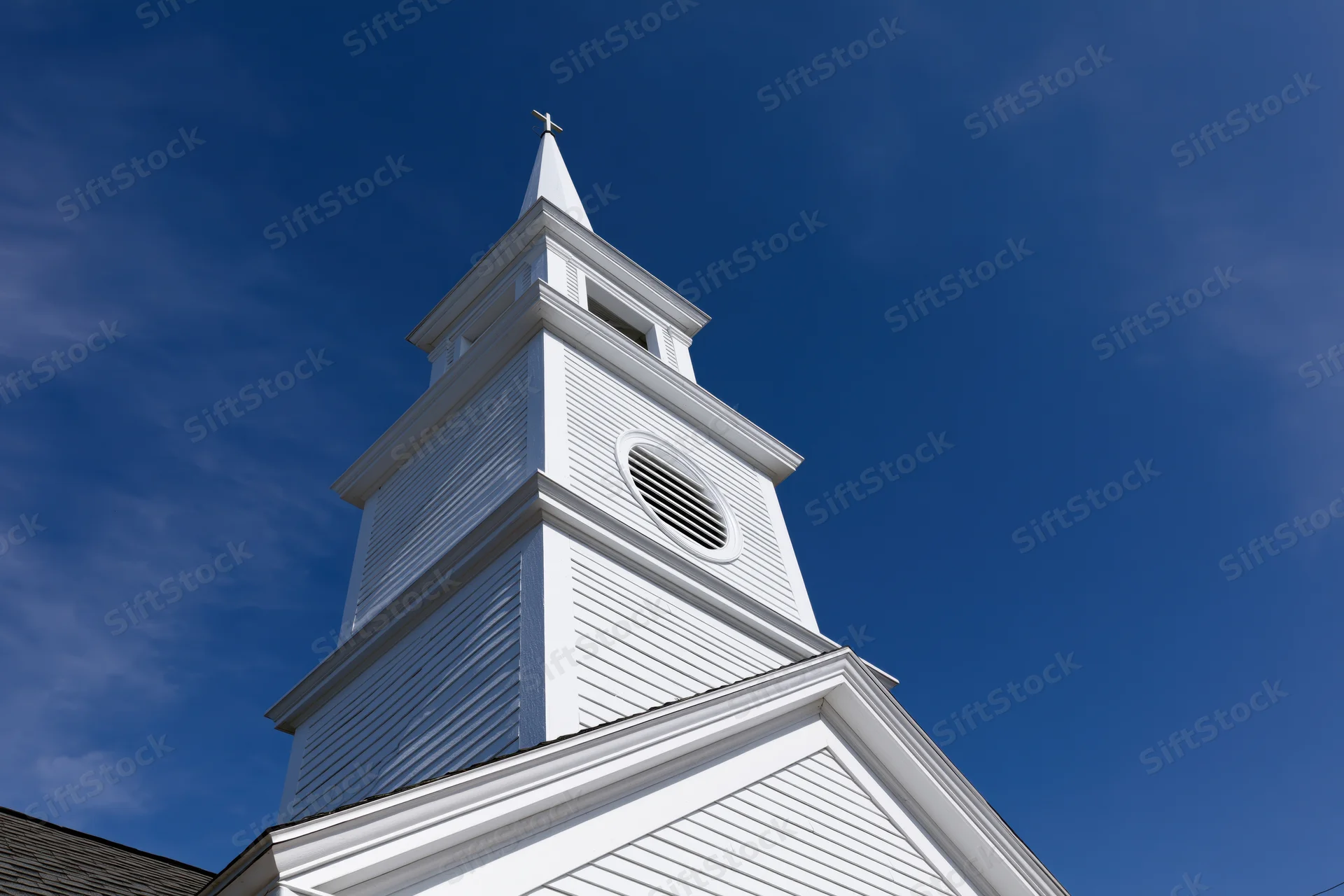 White church steeple with cross at peak against blue sky