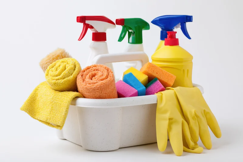 White plastic caddy filled with colorful cleaning supplies including spray bottles, sponges, cloths and rubber gloves