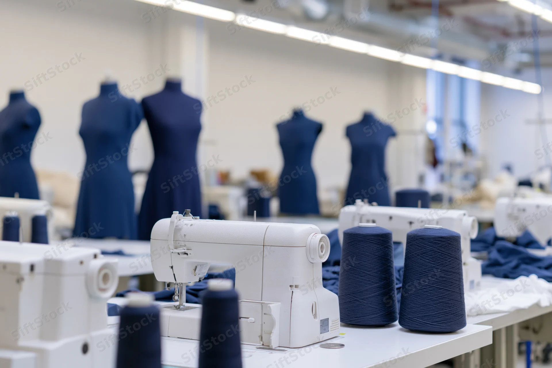 White sewing machines and blue thread spools on worktables in a garment factory