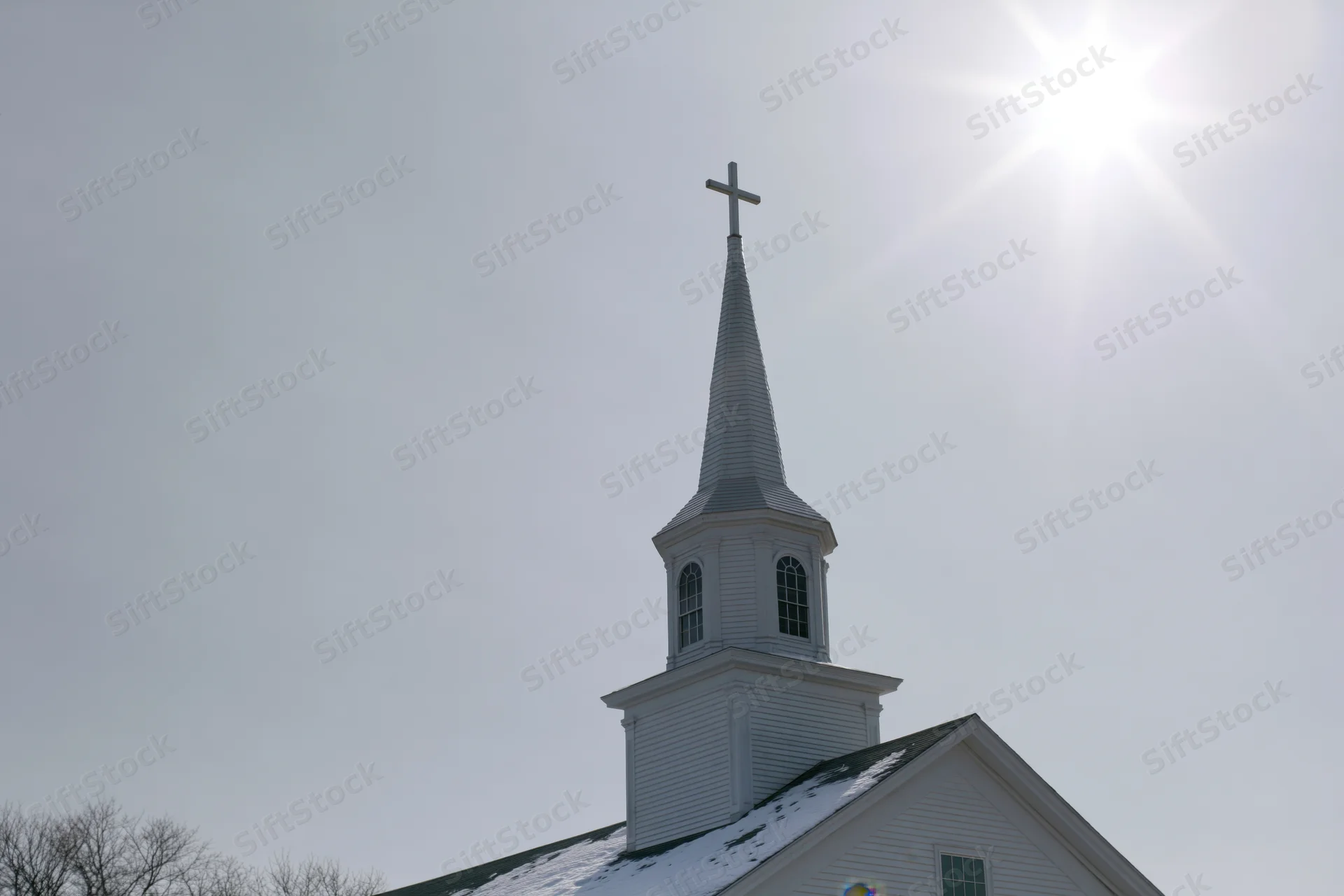 White wooden church steeple with cross against bright sunlit sky in winter