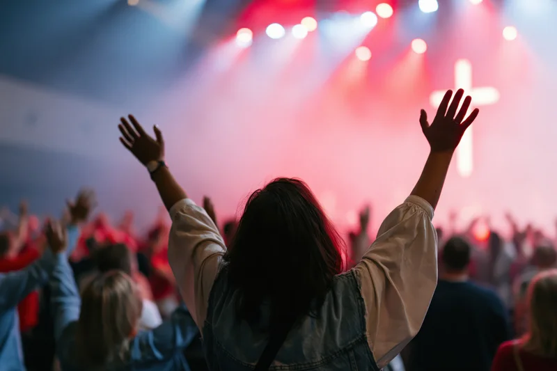 Woman with arms raised in worship facing a lit cross on stage during a church service
