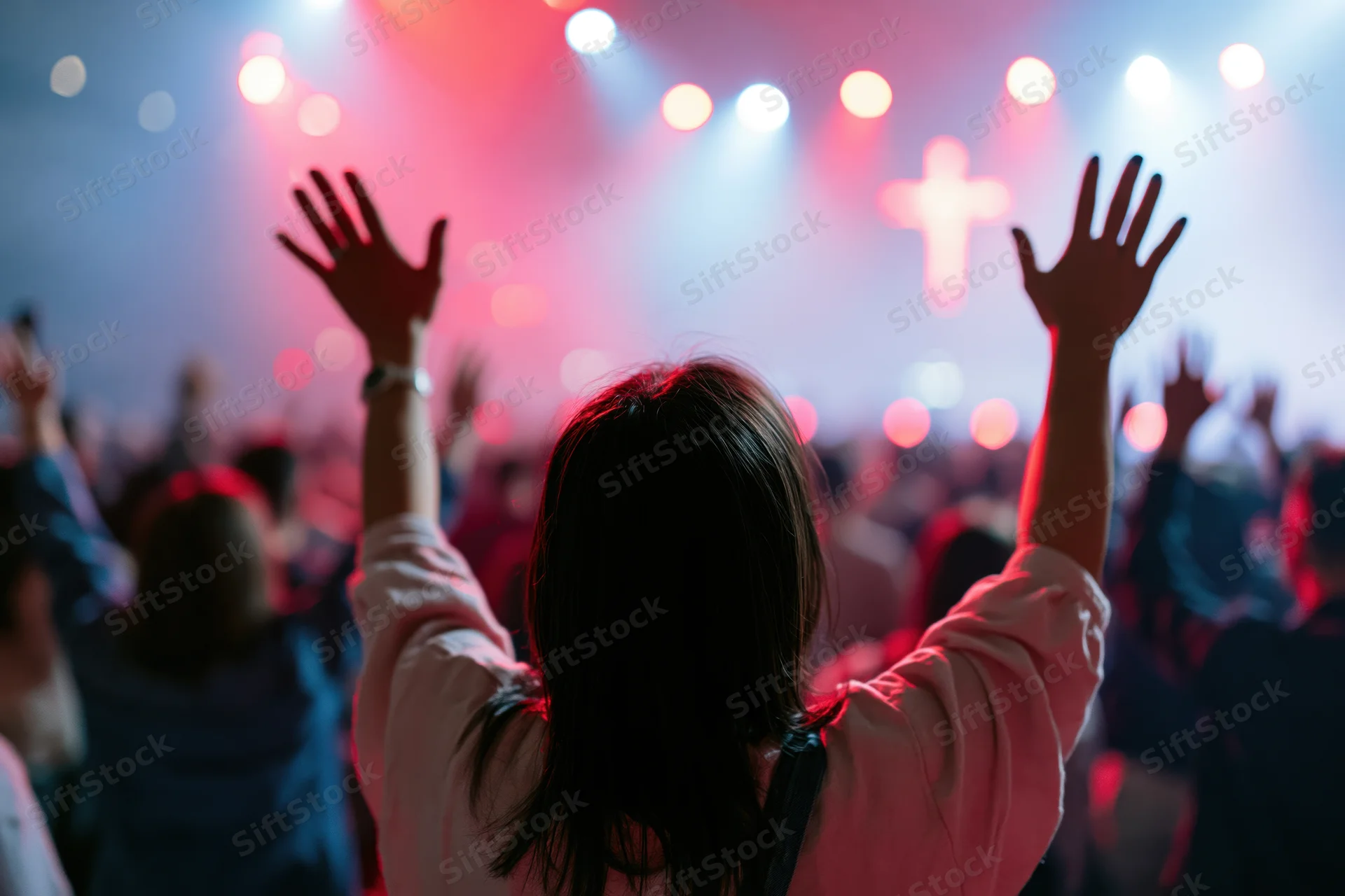 Woman raising hands in worship toward a lit cross on stage at a church service