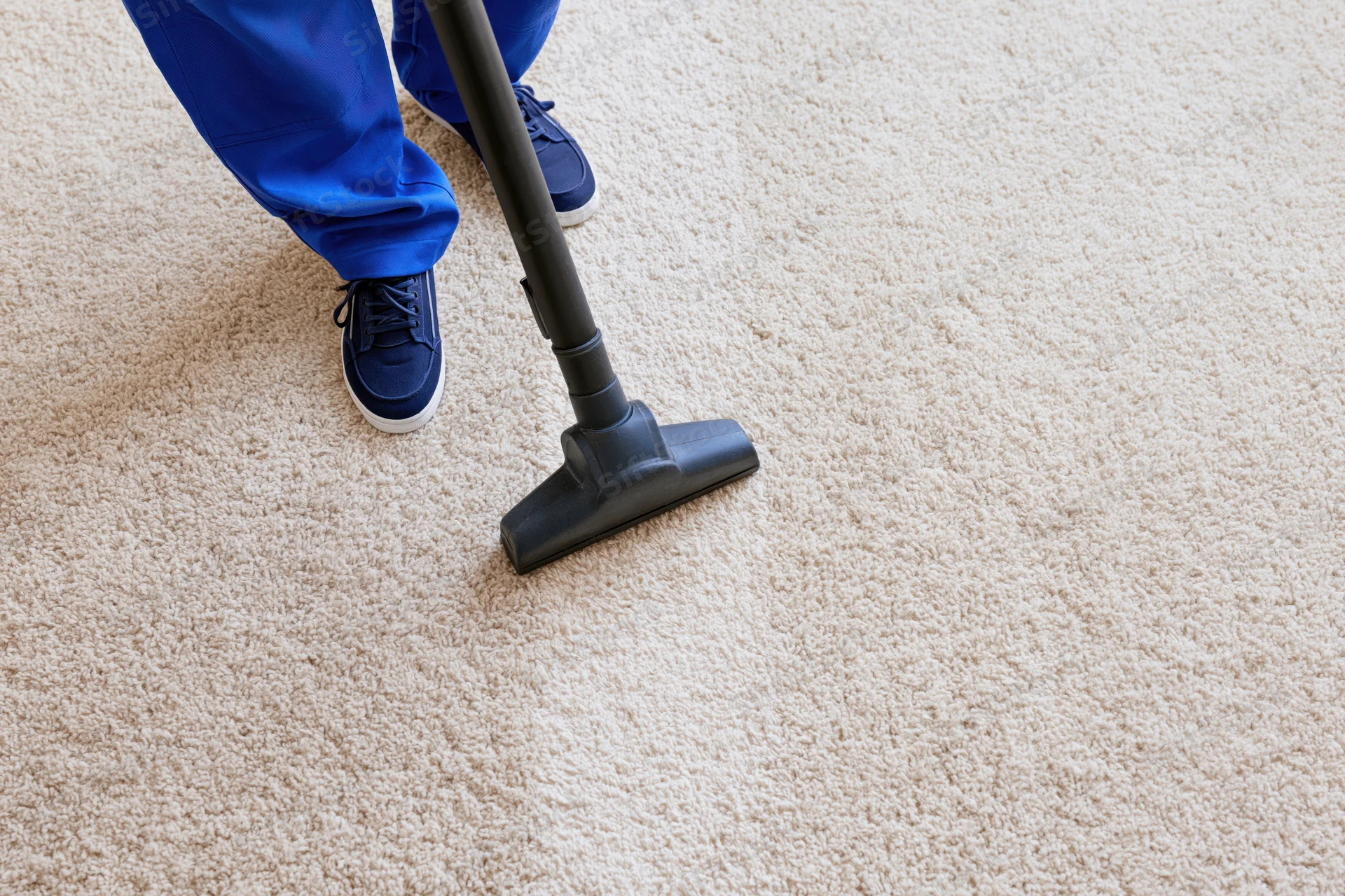 Worker vacuuming beige carpet in home interior
