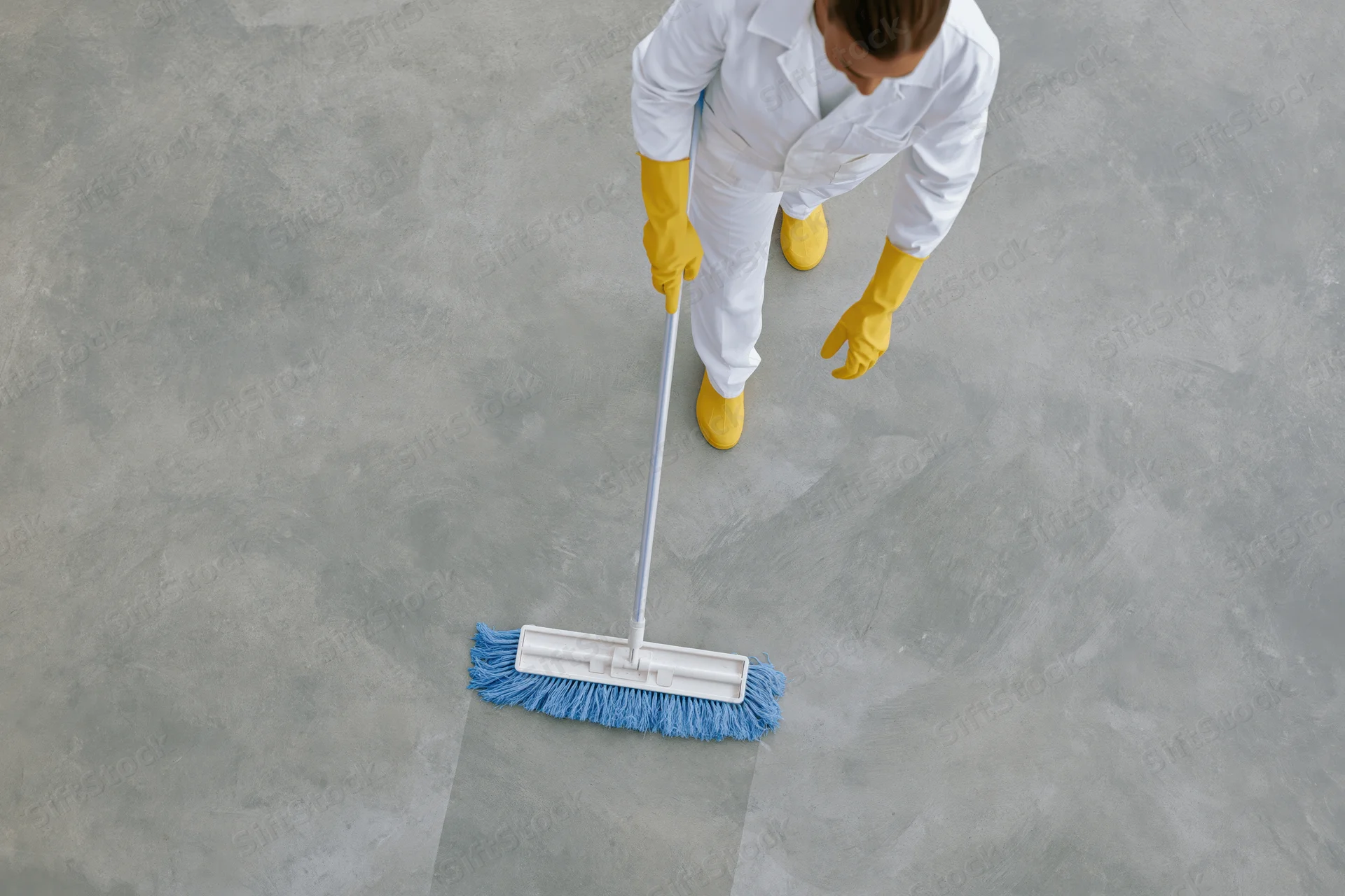 Worker in white uniform and yellow gloves mopping a concrete floor