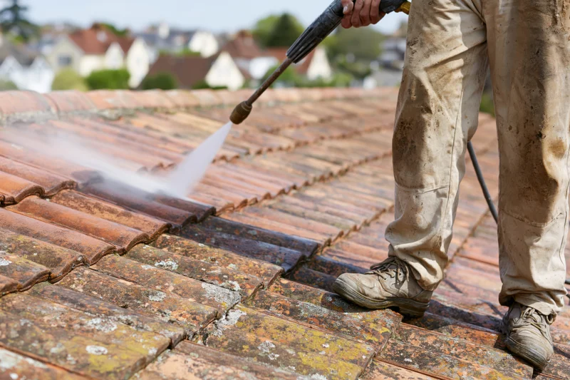 Worker pressure washing clay tile roof with spray nozzle on sloped residential exterior