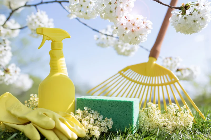 Yellow cleaning tools and garden rake arranged on grass beneath blooming cherry blossoms