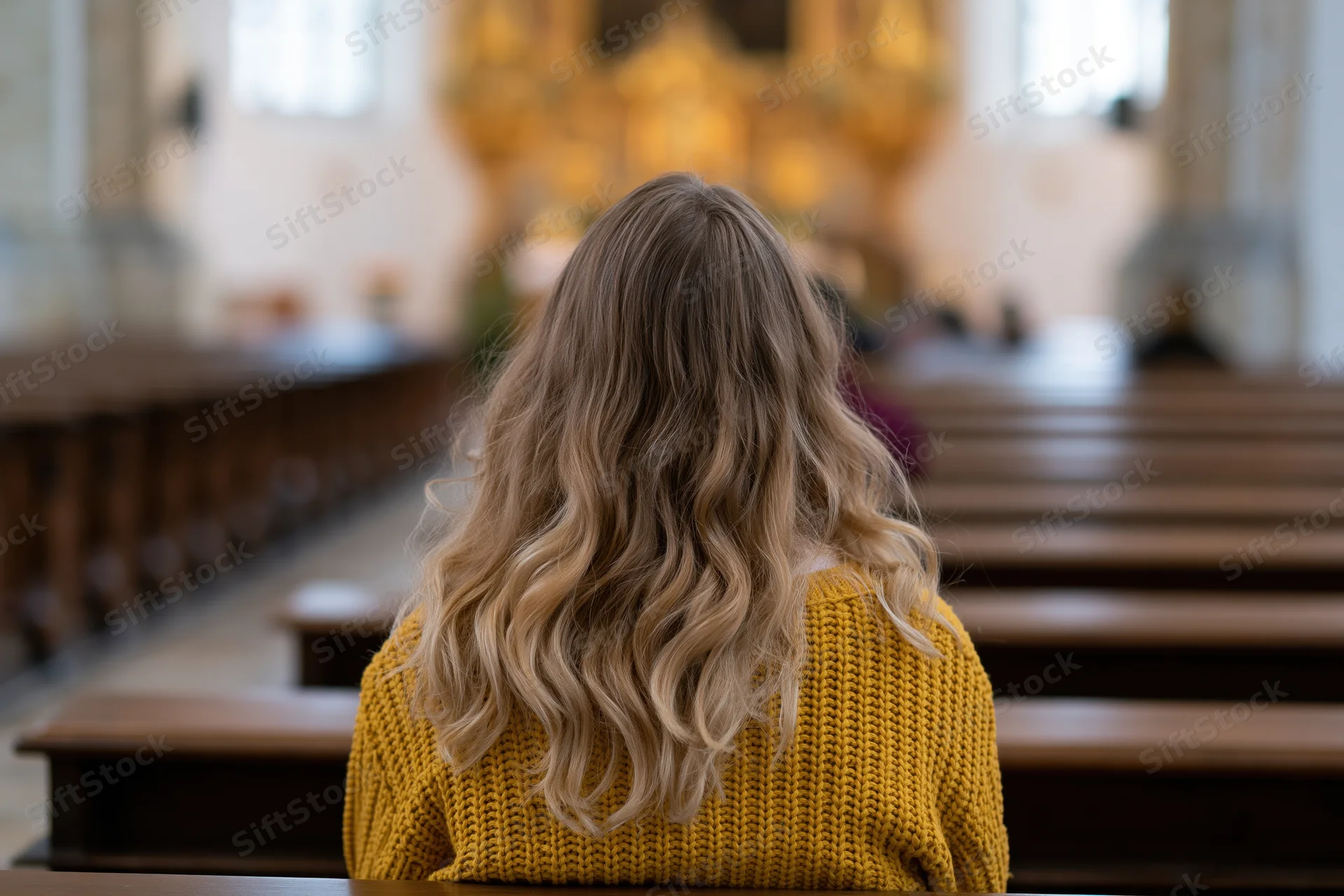 Woman with long wavy blonde hair sitting alone in church pews facing altar