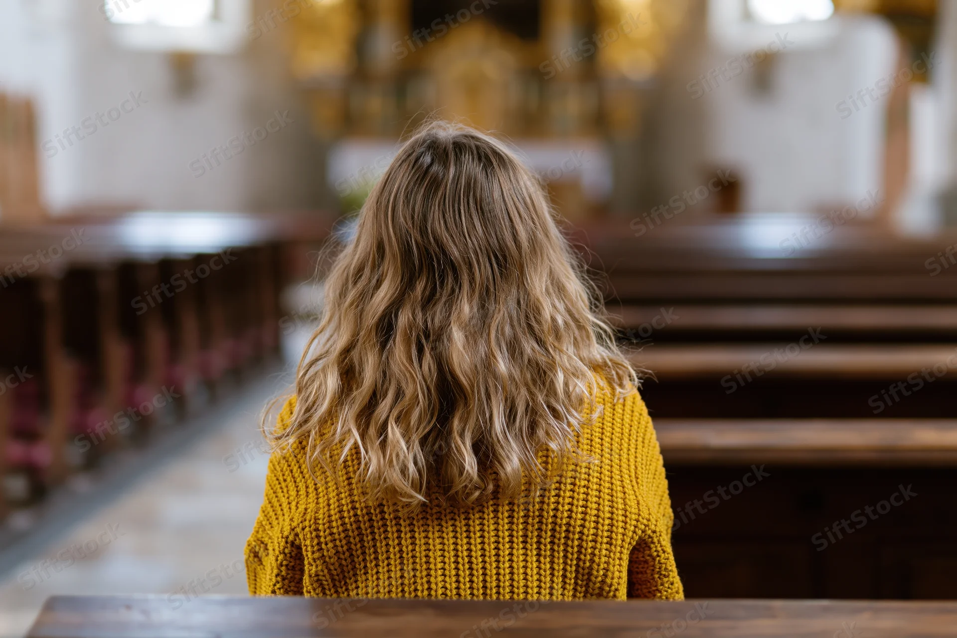 Woman with long wavy blonde hair sitting alone in a church facing the altar